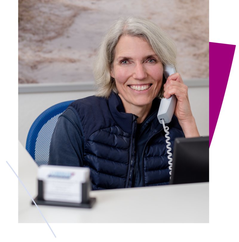 Kontakt Frau am Empfang mit Telefon in der Hand, lächelt freundlich. Heller Hintergrund und moderne Büroräume.